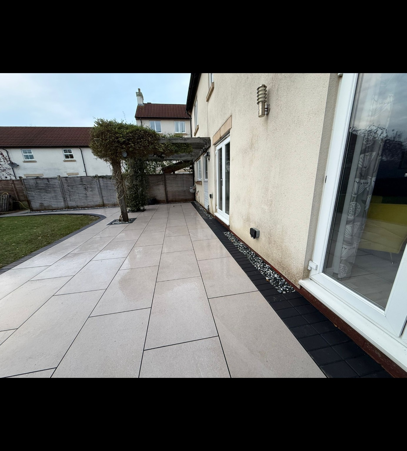 Light porcelain patio in Bridgwater with charcoal edging beside the house and curved lawn