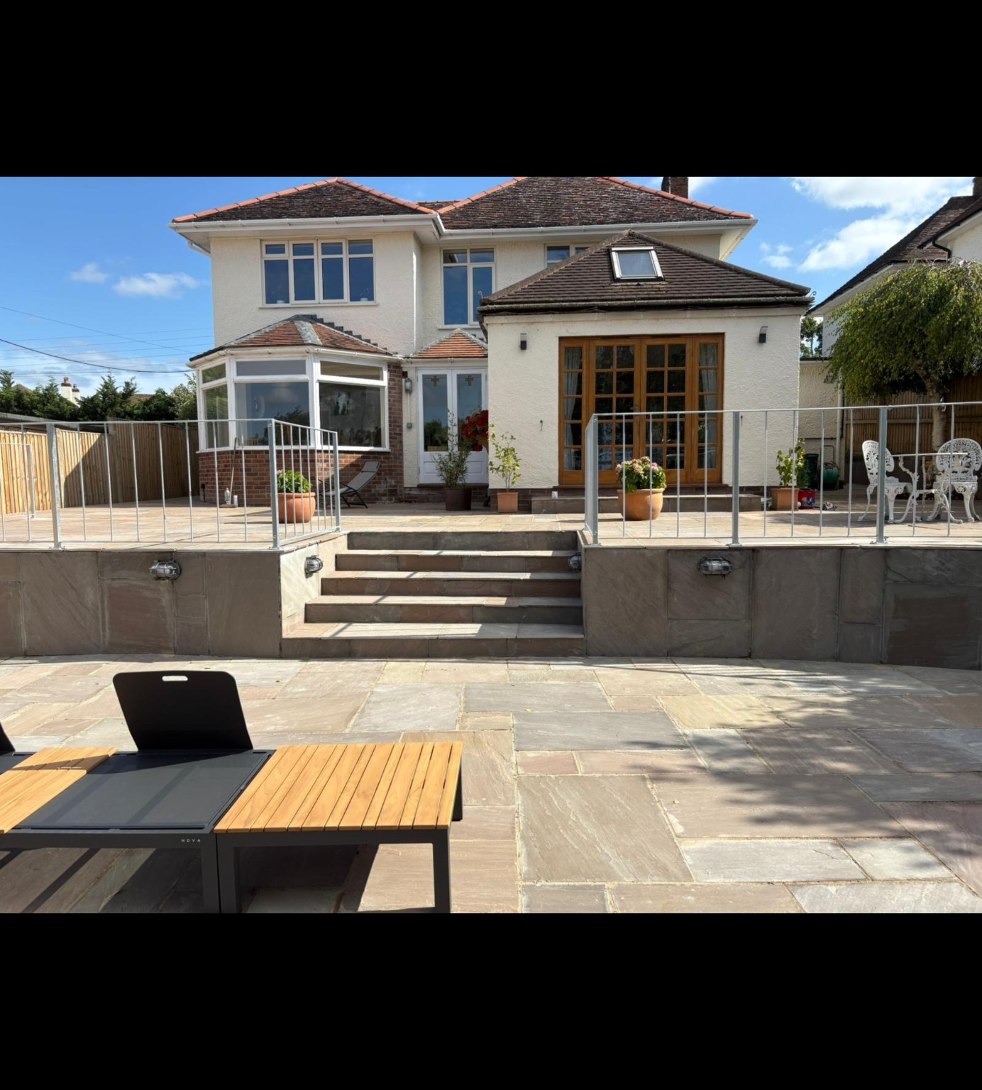 Mr Hayman’s completed Indian sandstone patio in Taunton with galvanised railings, central steps, wall lights and outdoor dining space
