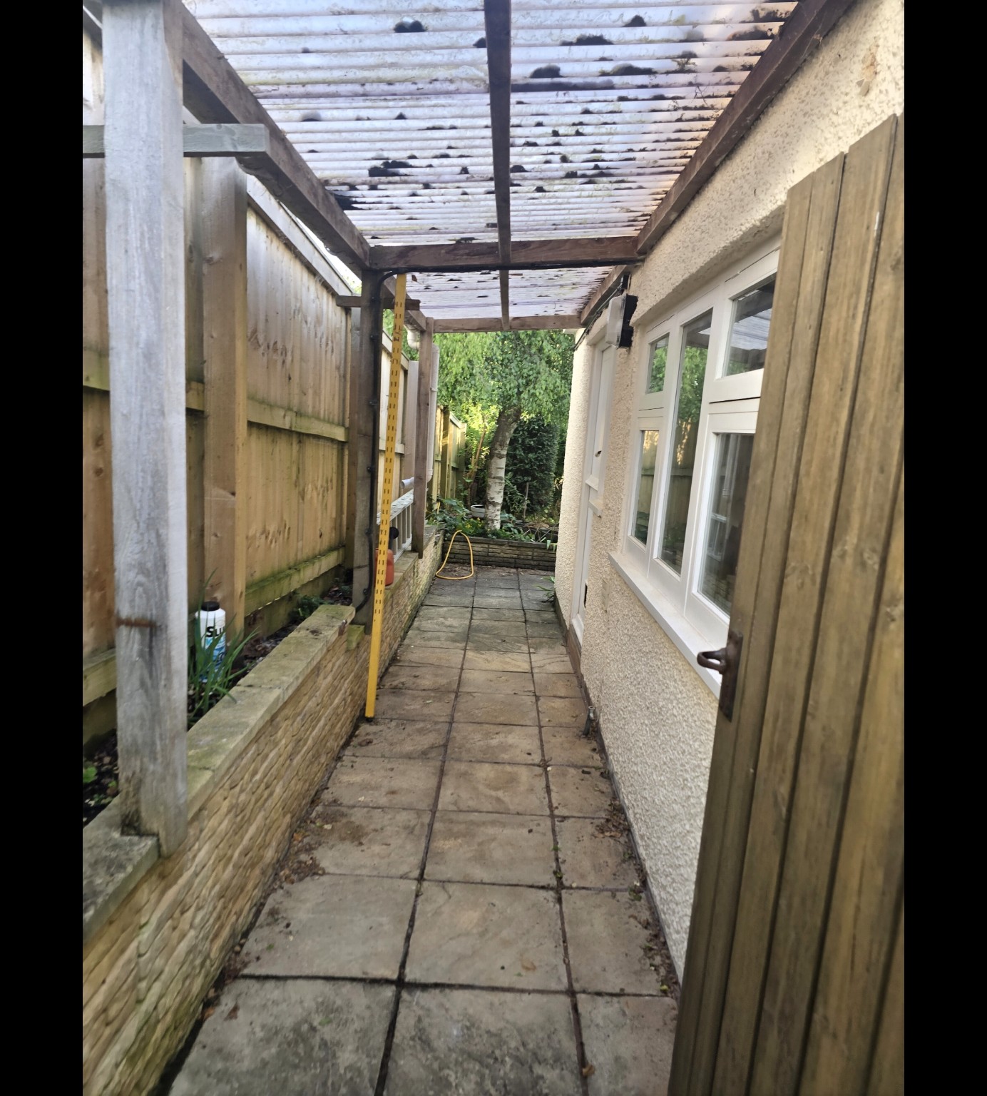 Existing narrow paved passage, timber canopy and boundary fence before work in Taunton