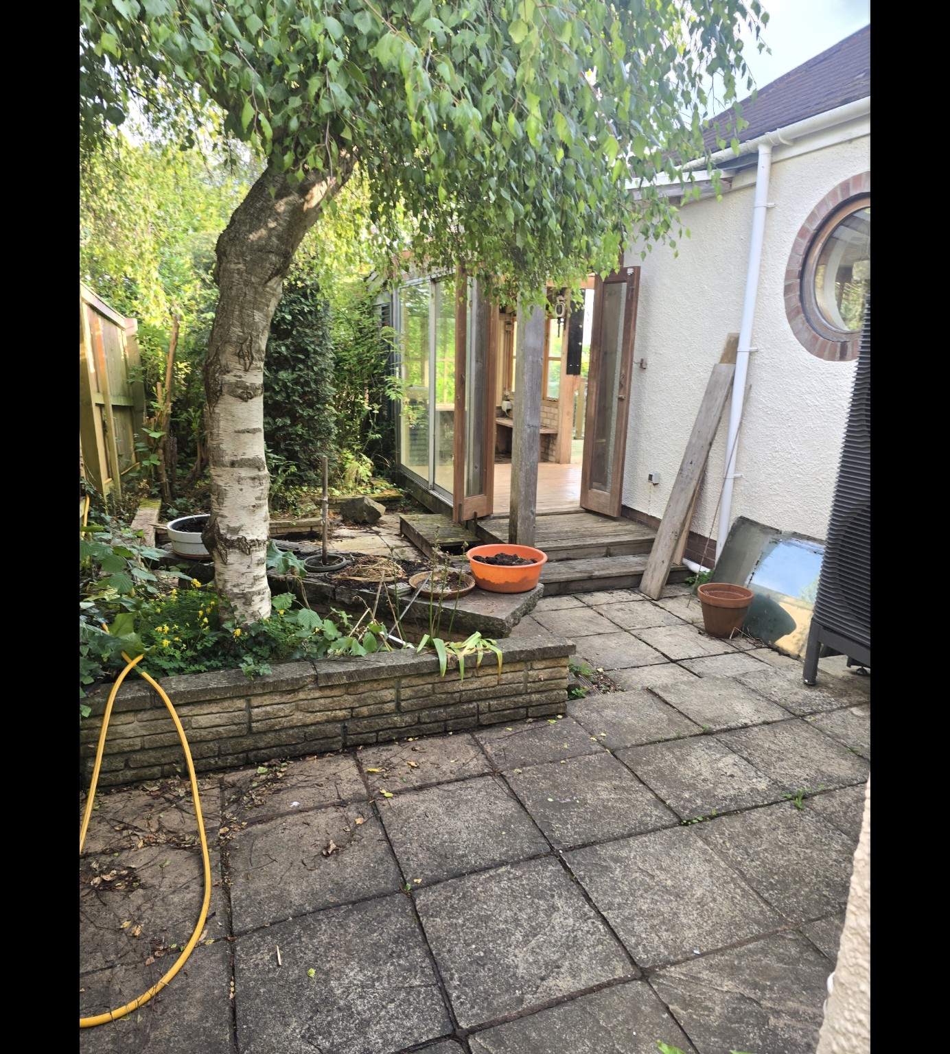 Old paving and timber structures around the retained tree before the Taunton patio transformation