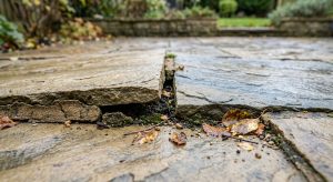 Uneven sandstone patio slabs with a cracked open joint caused by ground movement